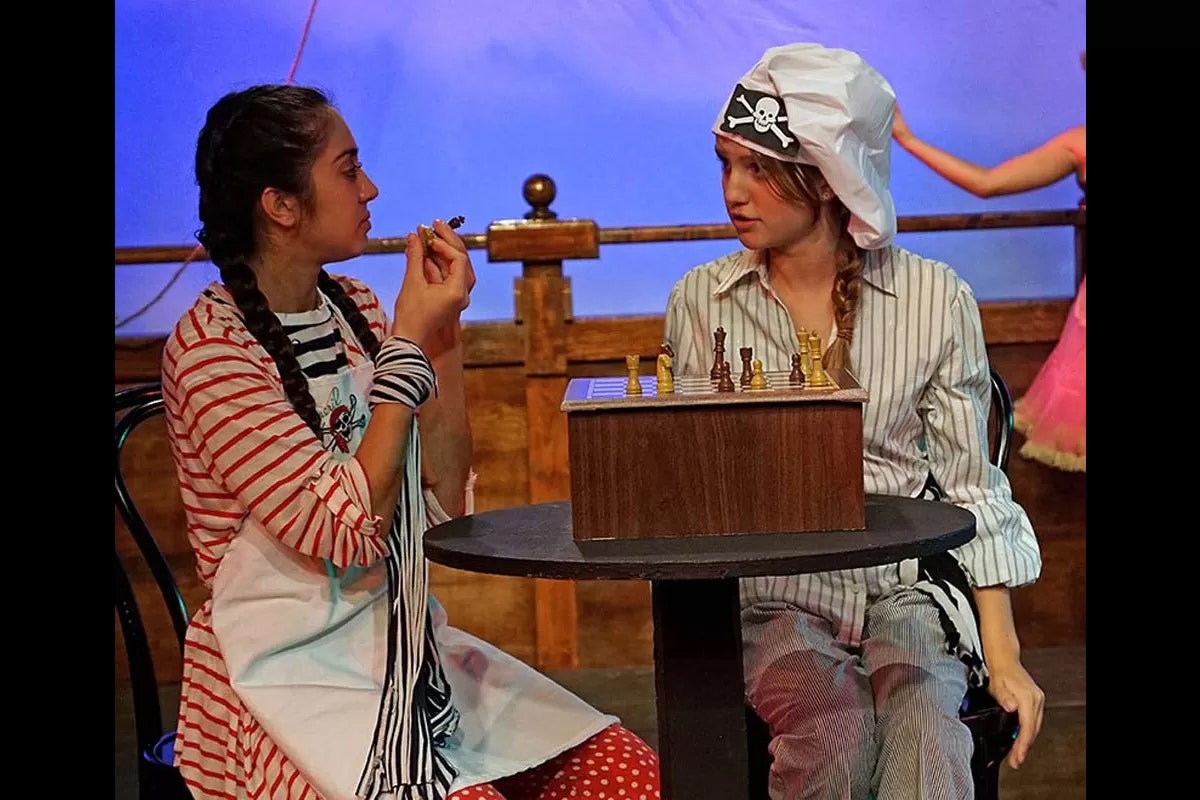 Two people in costume by a table with a chessboard. One has a pirate hat, the other holds a chess piece.