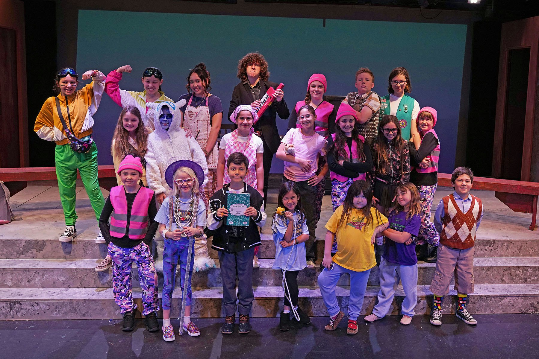 A vibrant group of kids in colorful costumes poses on stage, showcasing a fun theatrical performance.