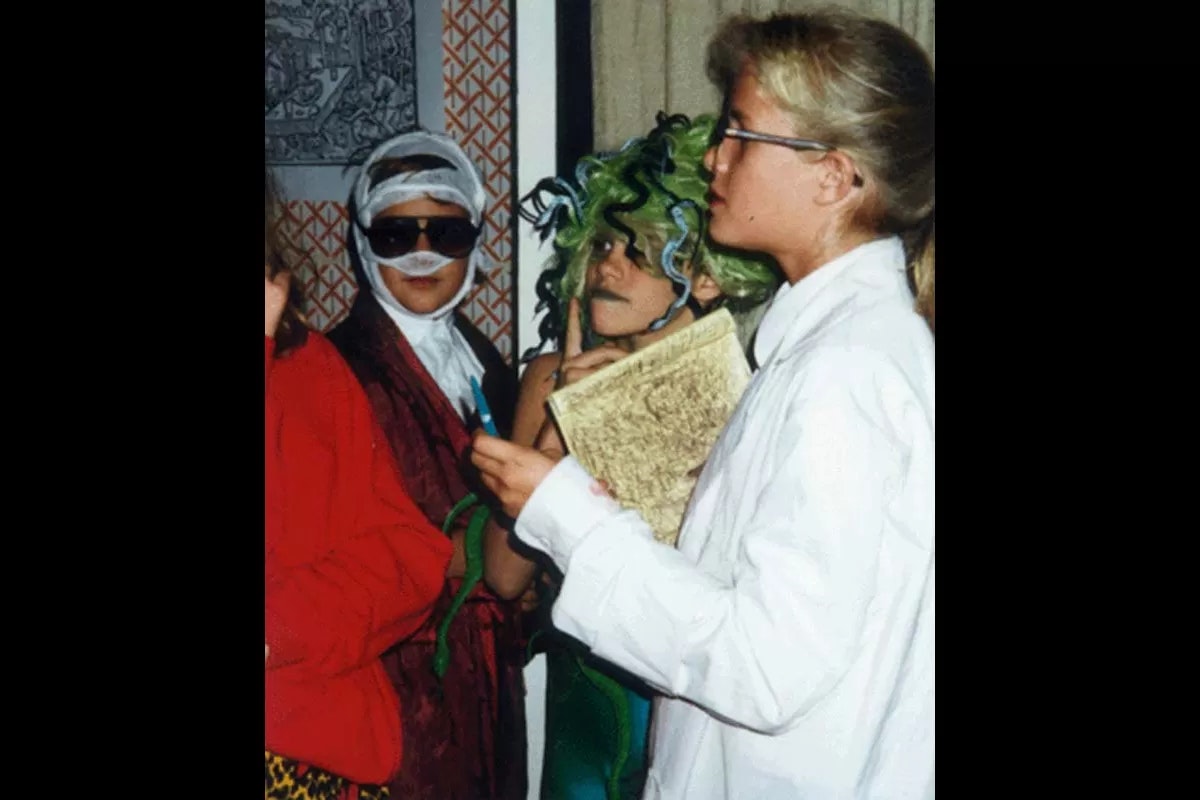 Three people in costumes, one with a notebook, another with a green snake wig, and the third in sunglasses and a bandaged head.