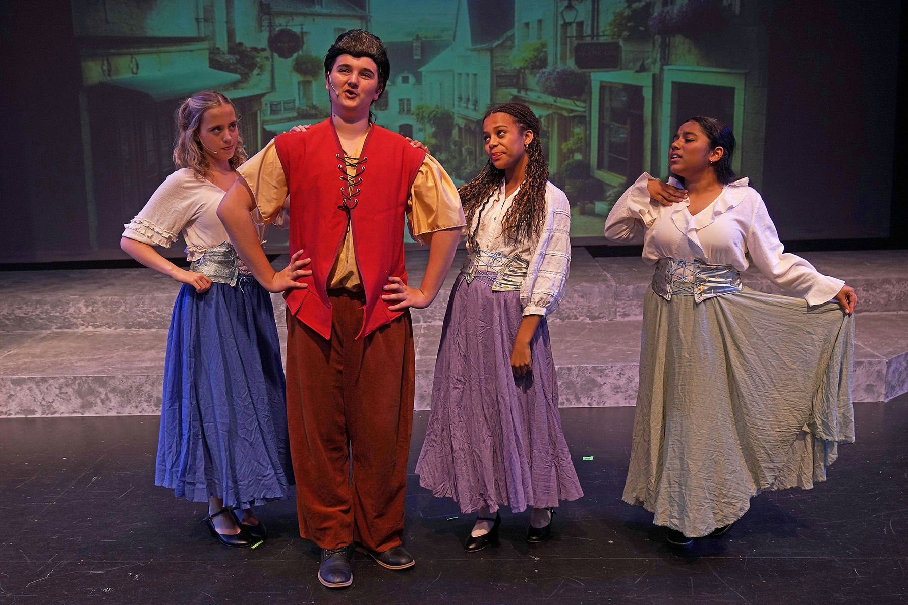 Four actors on stage in period costumes, posing with a village backdrop.