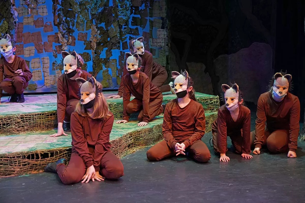 People in animal masks and brown costumes crouch on a decorated stage.