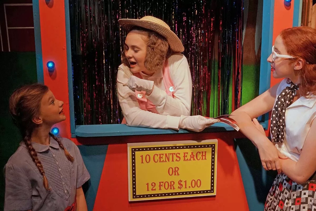 Three people talking at a colorful booth. The sign reads "10 cents each or 12 for $1.00."