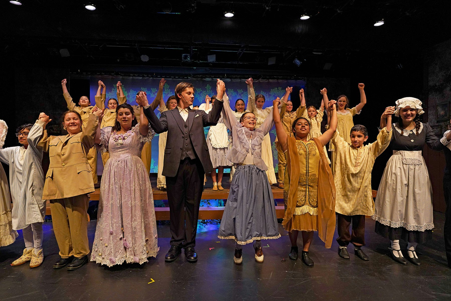 A group of people in period costumes on stage, raising their hands in celebration or taking a bow.