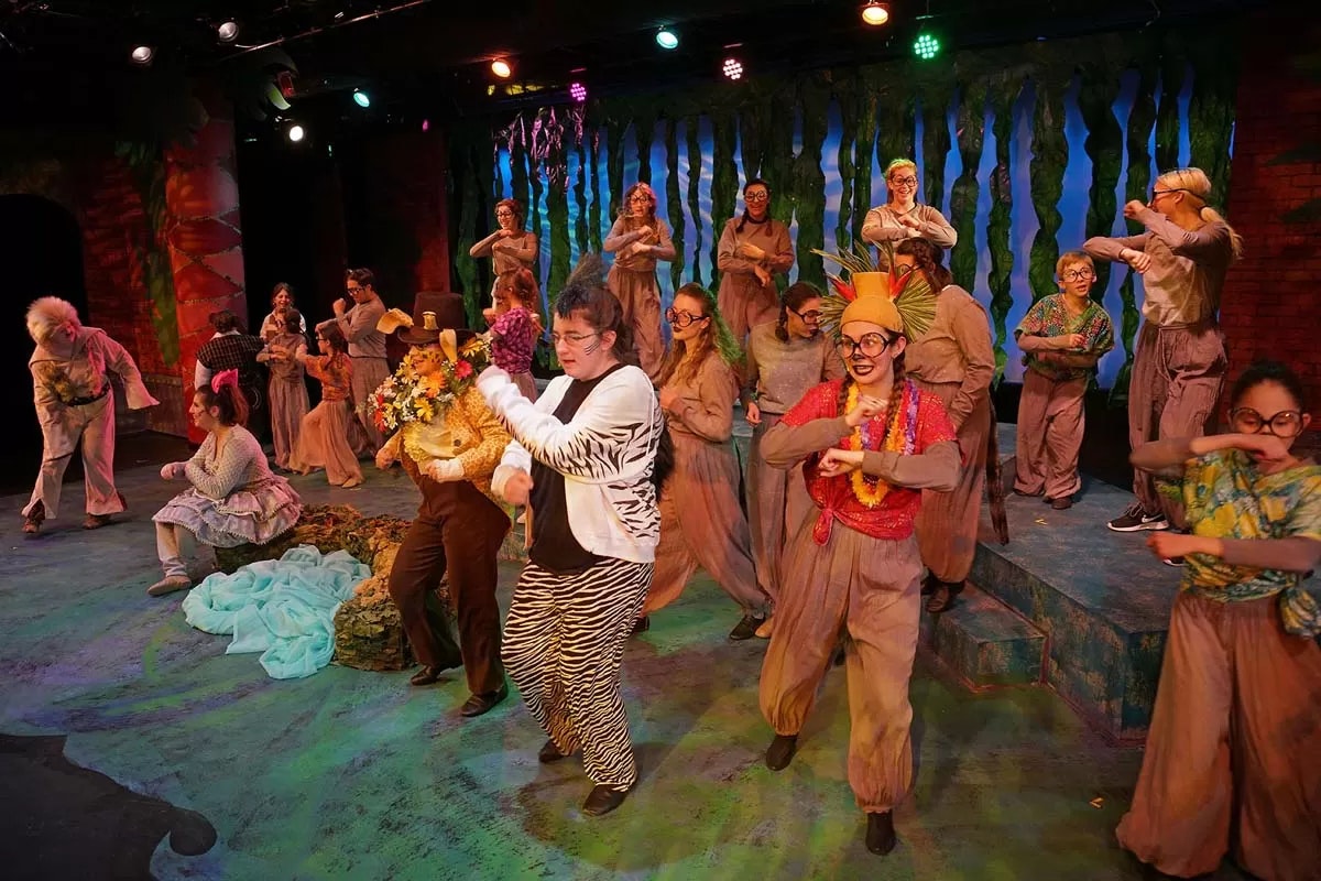 A stage performance with actors in colorful costumes dancing energetically.
