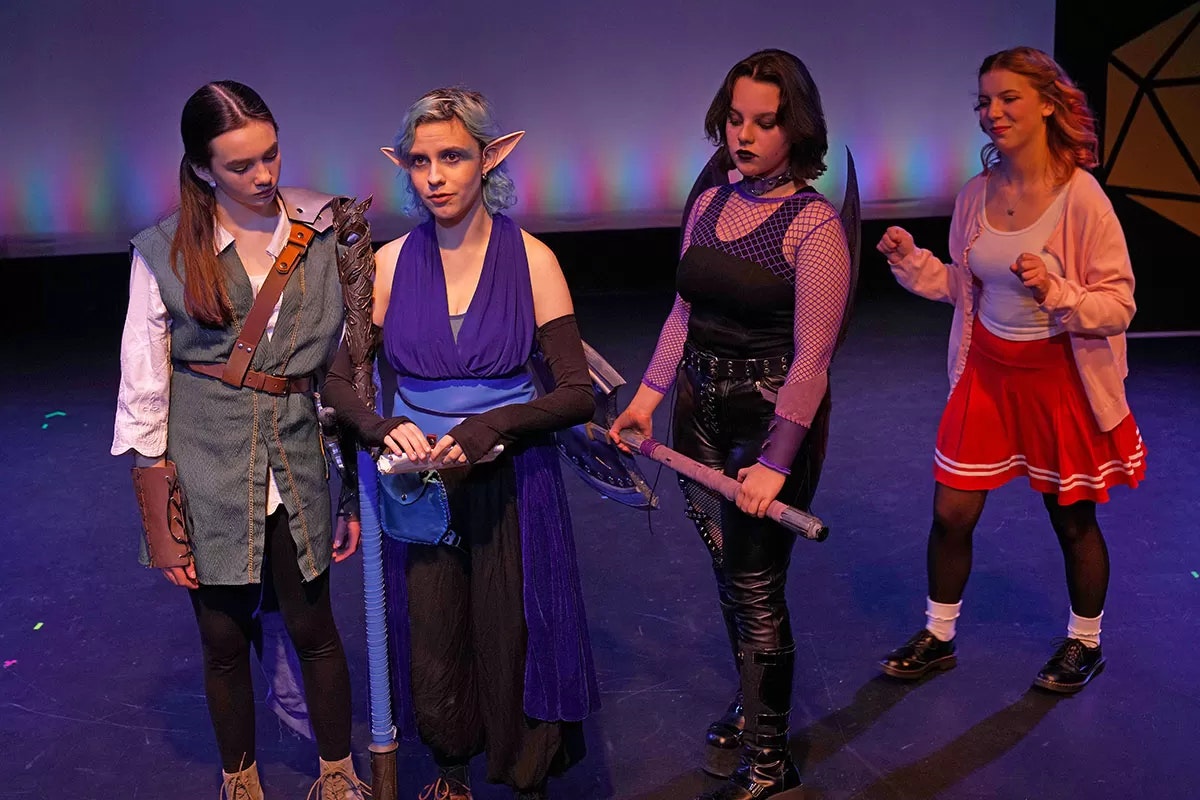 Four people in fantasy costumes stand on a stage, engaged in a scene.