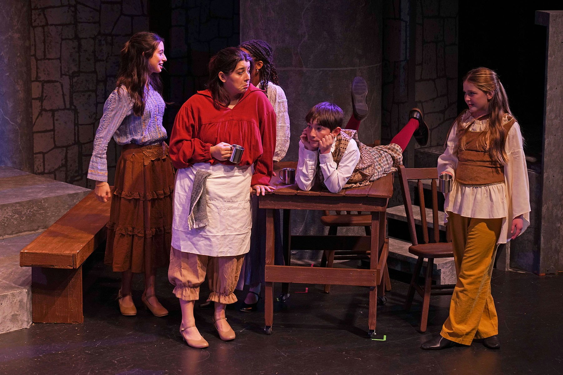 A group of people in period costumes performing on stage, with one person lying on a table.