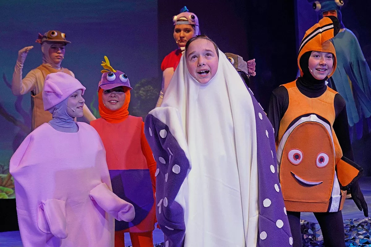 Children dressed in colorful sea creature costumes on stage, performing in a play.
