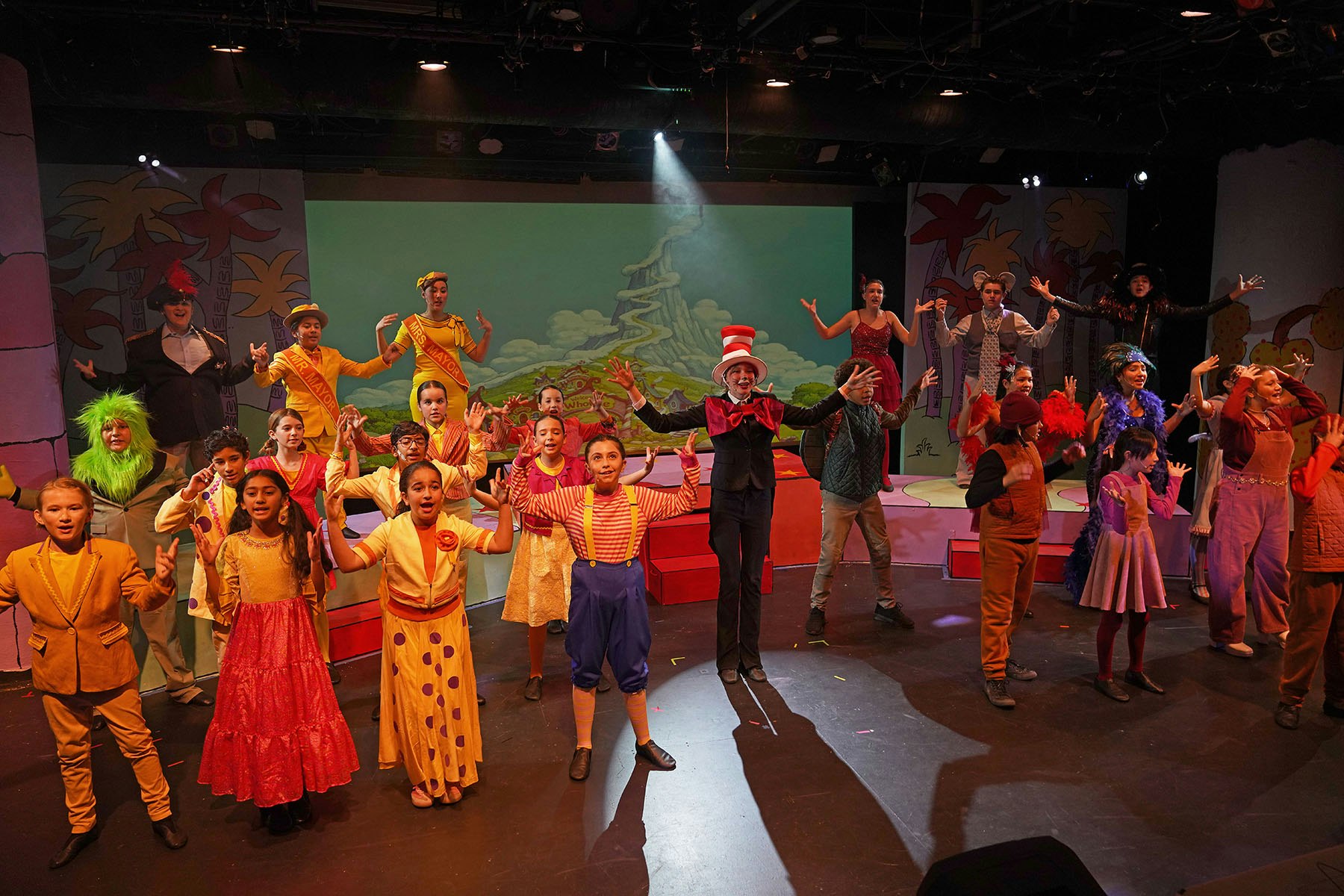 A group of children perform on stage in colorful costumes, likely from a theatrical production inspired by a Dr. Seuss story.