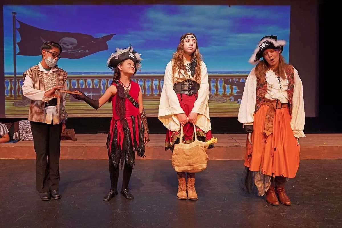 Four children in pirate costumes performing on stage with a pirate ship backdrop.