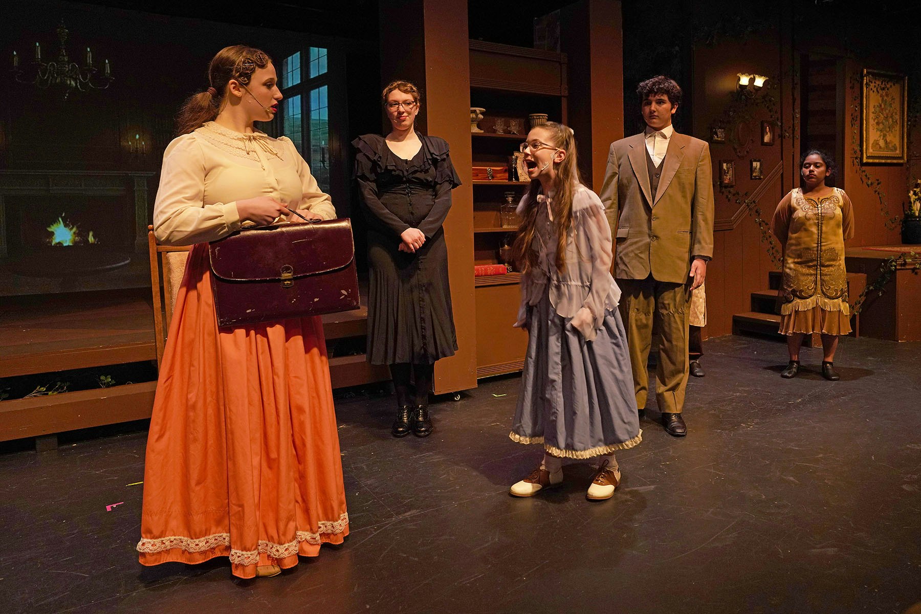Five people in period costumes are performing on a stage with a vintage setting.