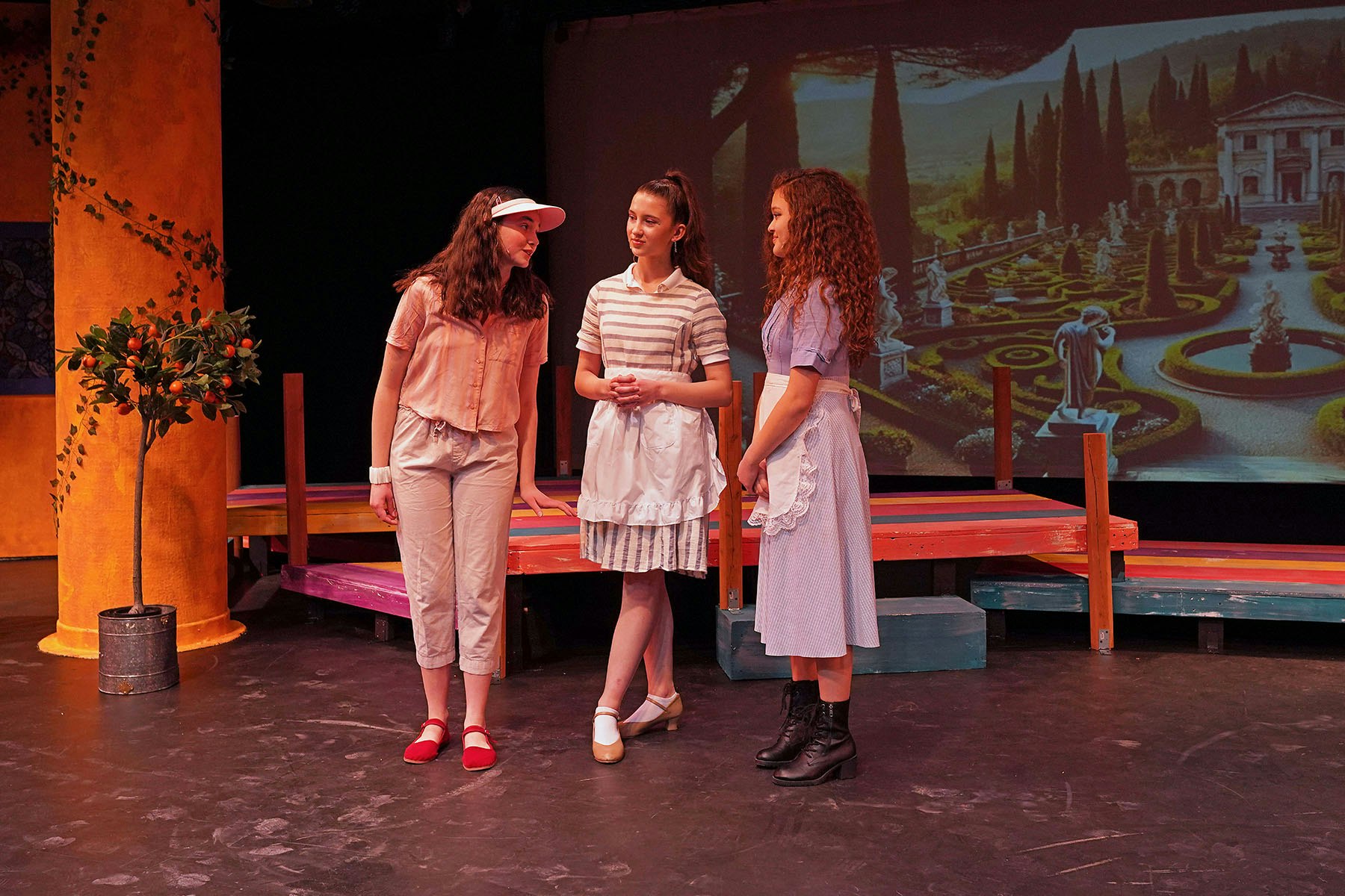 Three people on stage in costume, a backdrop of a garden.