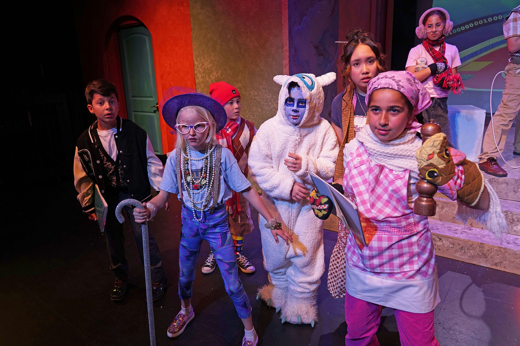 A group of children in colorful costumes performing on stage, showcasing diverse characters and expressions.