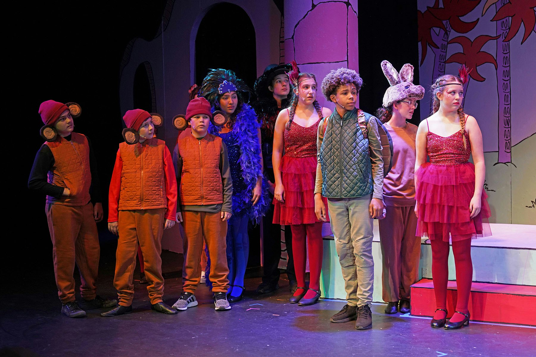 A group of children performing on stage, wearing colorful costumes with whimsical elements, showcasing a theatrical production.