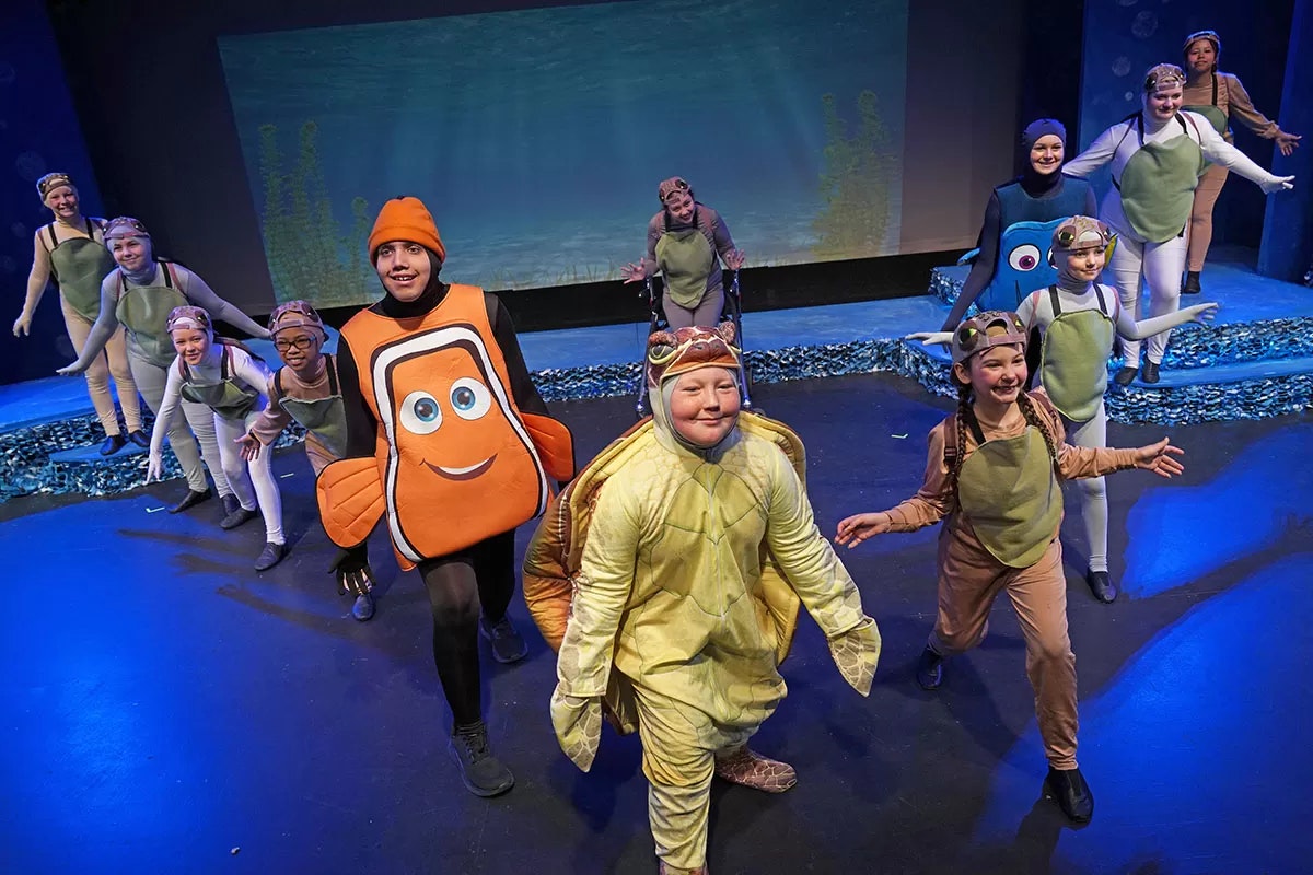 Children in colorful ocean-themed costumes performing on stage.