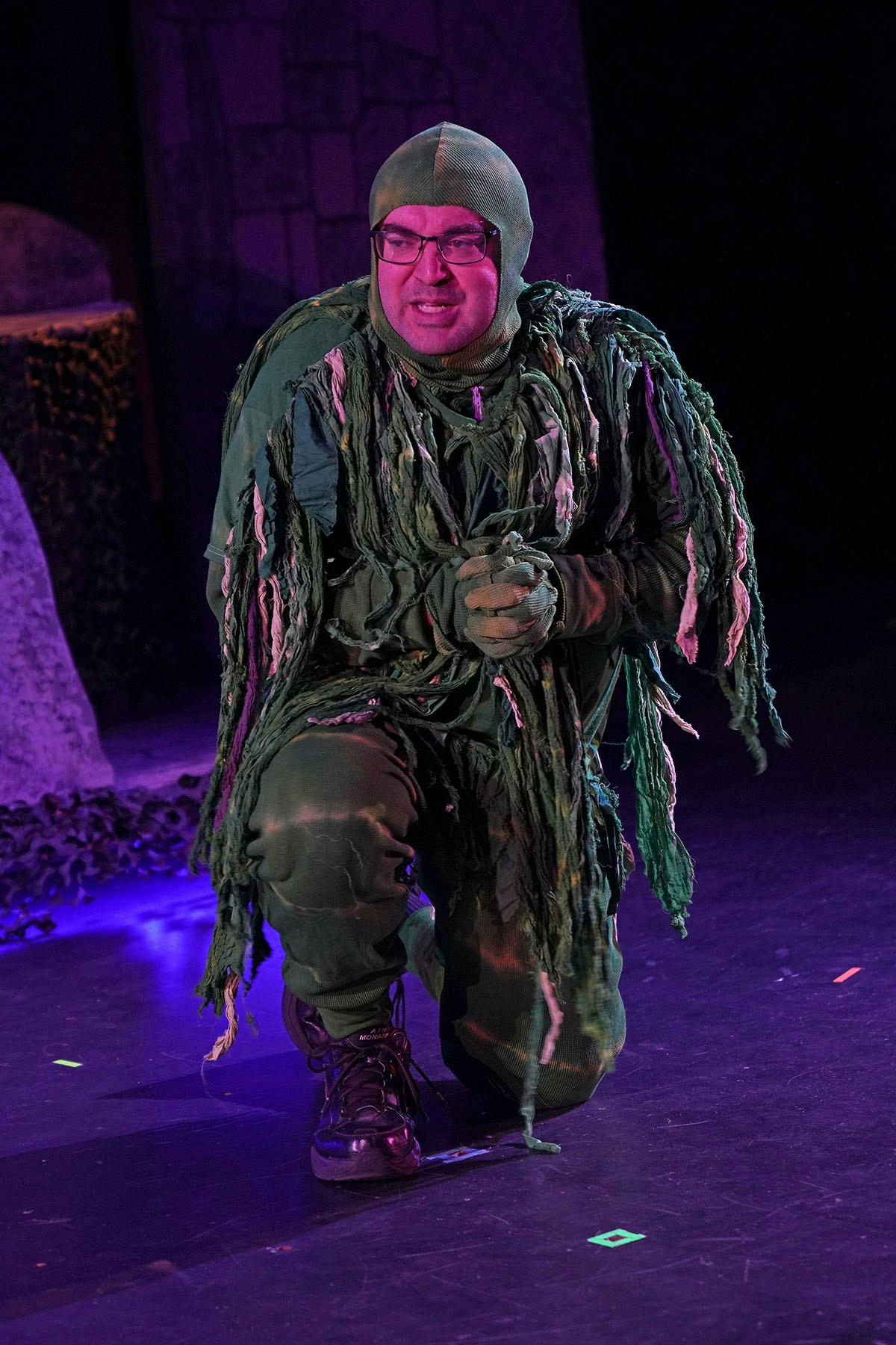 A person in a green leafy costume kneeling on stage, smiling.