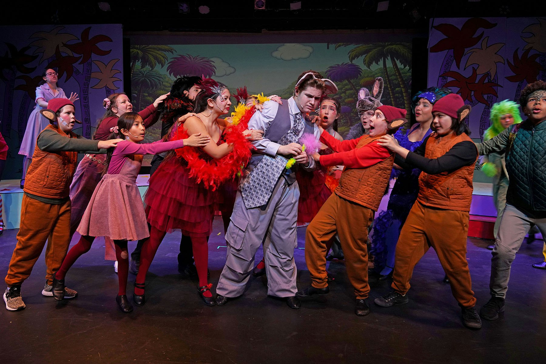 A lively theatrical performance featuring a diverse cast in colorful costumes, engaged in an expressive group scene.