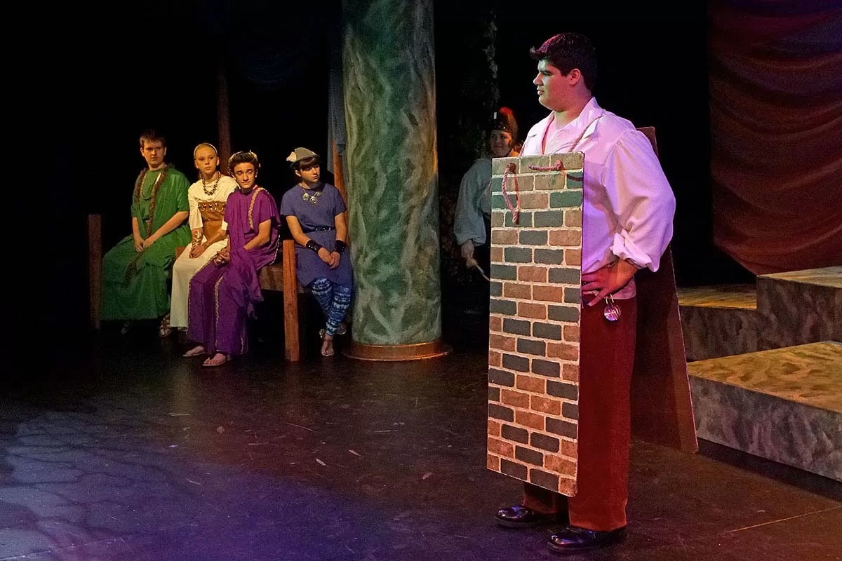 A group of people in costumes on stage; one person is dressed as a brick wall.