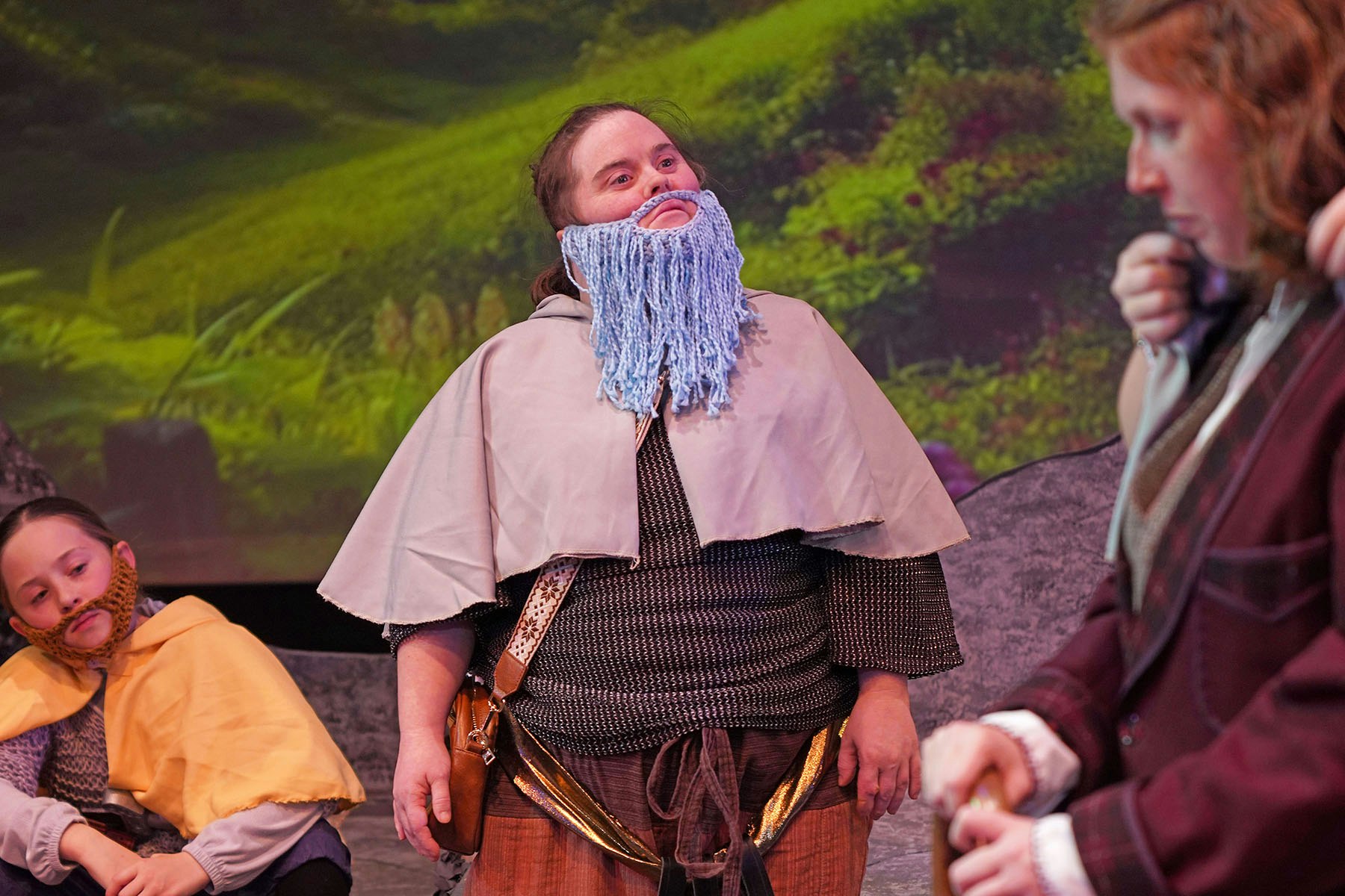 People in costumes wearing yarn beards, possibly in a theatrical setting with a forest backdrop.