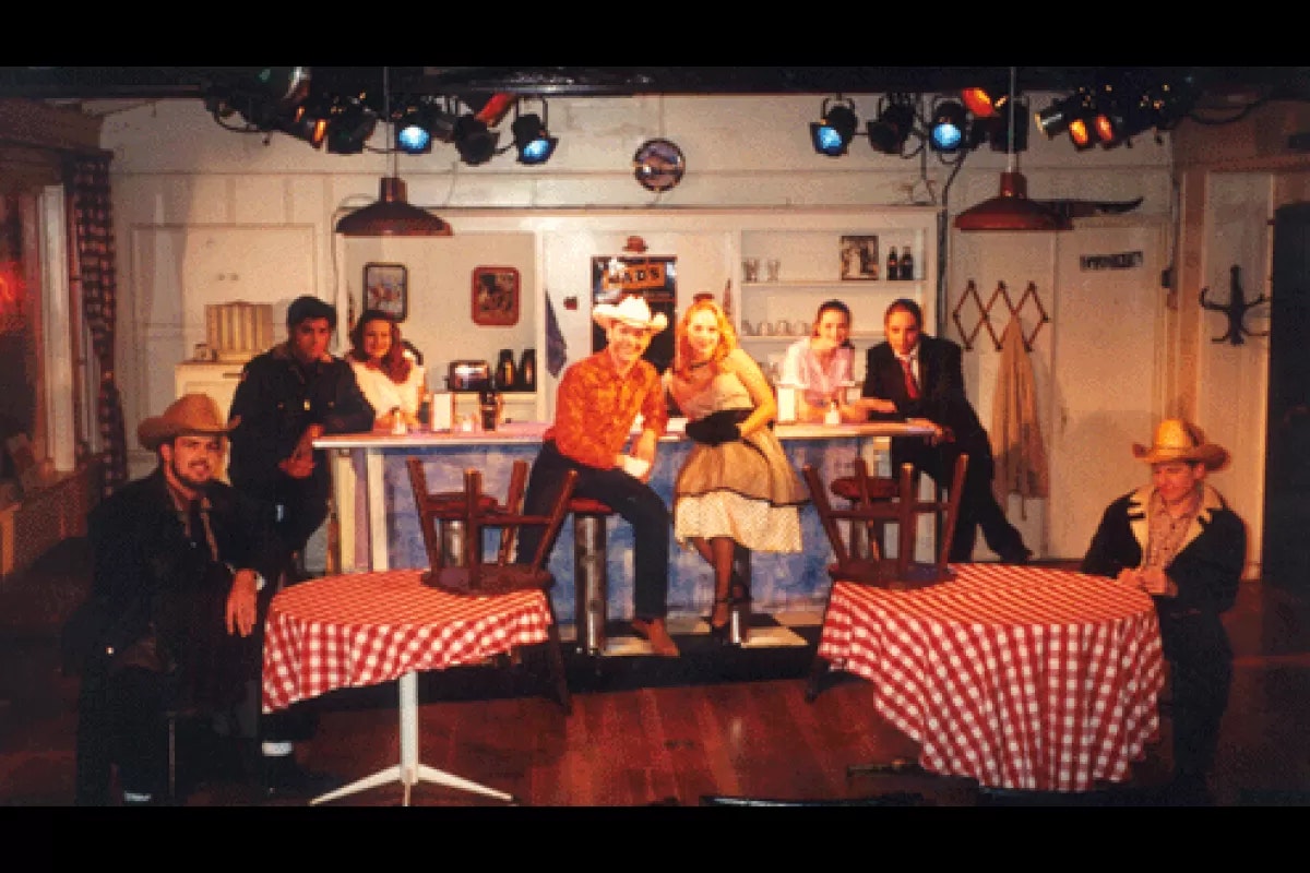 People dressed in retro attire on a diner-themed stage, with tables covered in checkered tablecloths.
