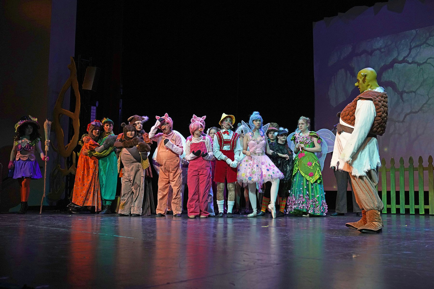 A group of people in colorful fairytale costumes on stage, possibly in a theater performance.