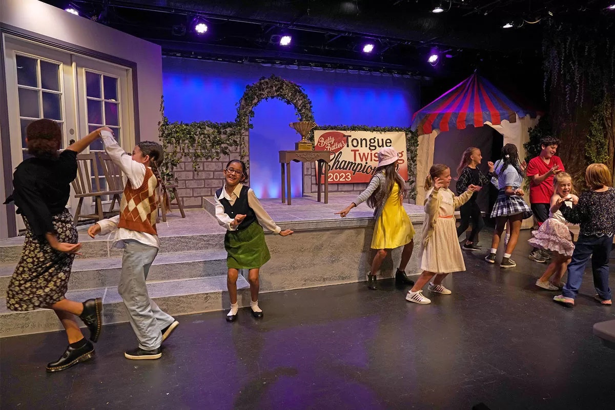 Children dancing on stage with a "Tongue Twisters Championship 2023" sign in the background.
