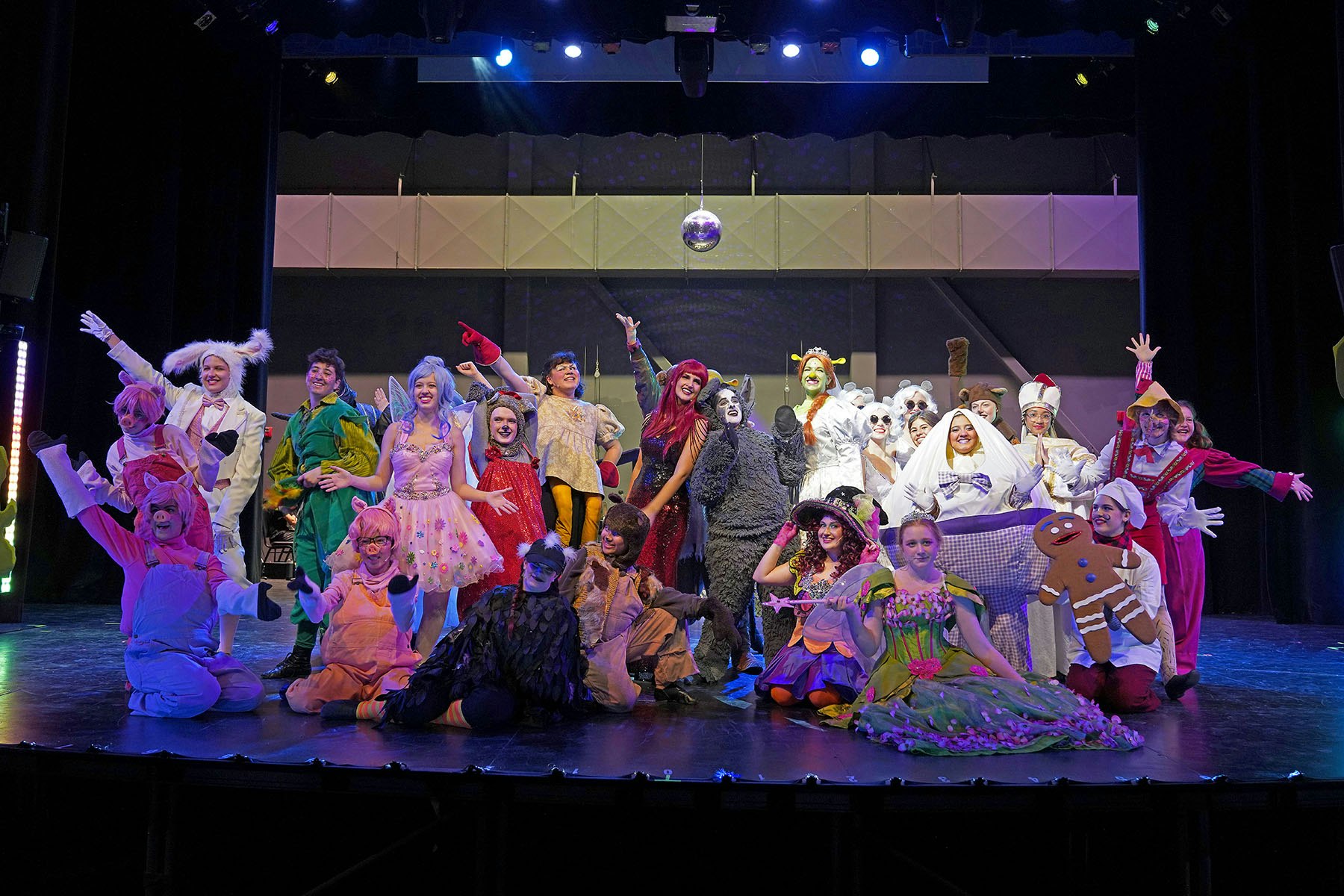 A group of people in colorful costumes posing on a stage, under a disco ball.