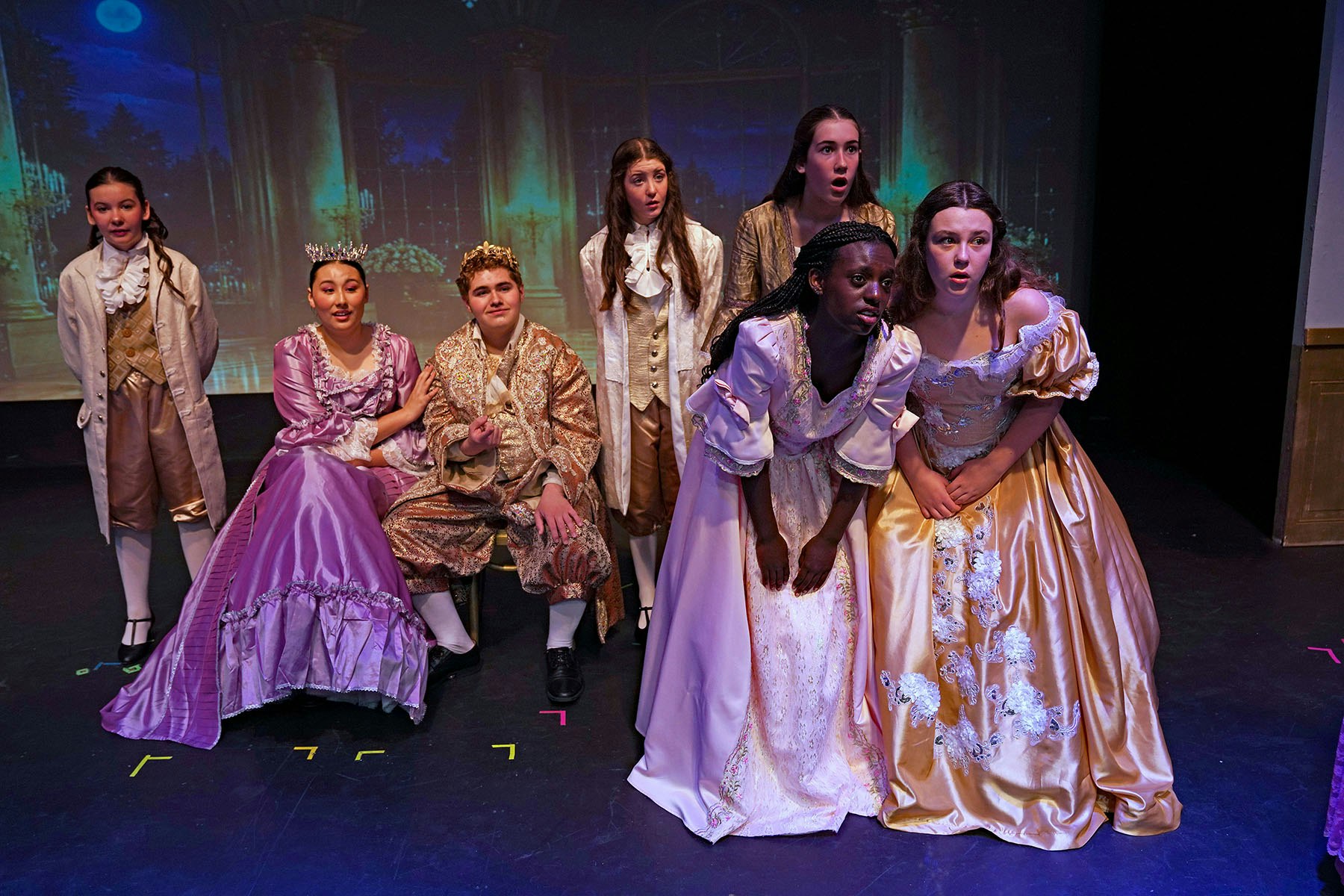 A group of young performers dressed in historical costumes, likely in a theatrical production, with varied expressions.
