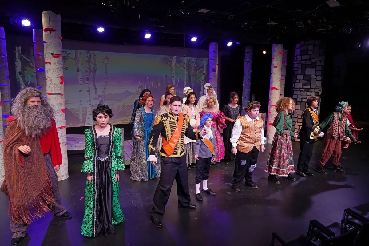 A theater performance with a group of actors in colorful, period costumes on stage.