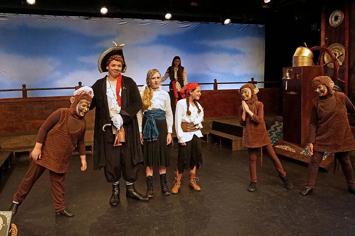 A theatrical scene with actors dressed as pirates and monkeys on stage.