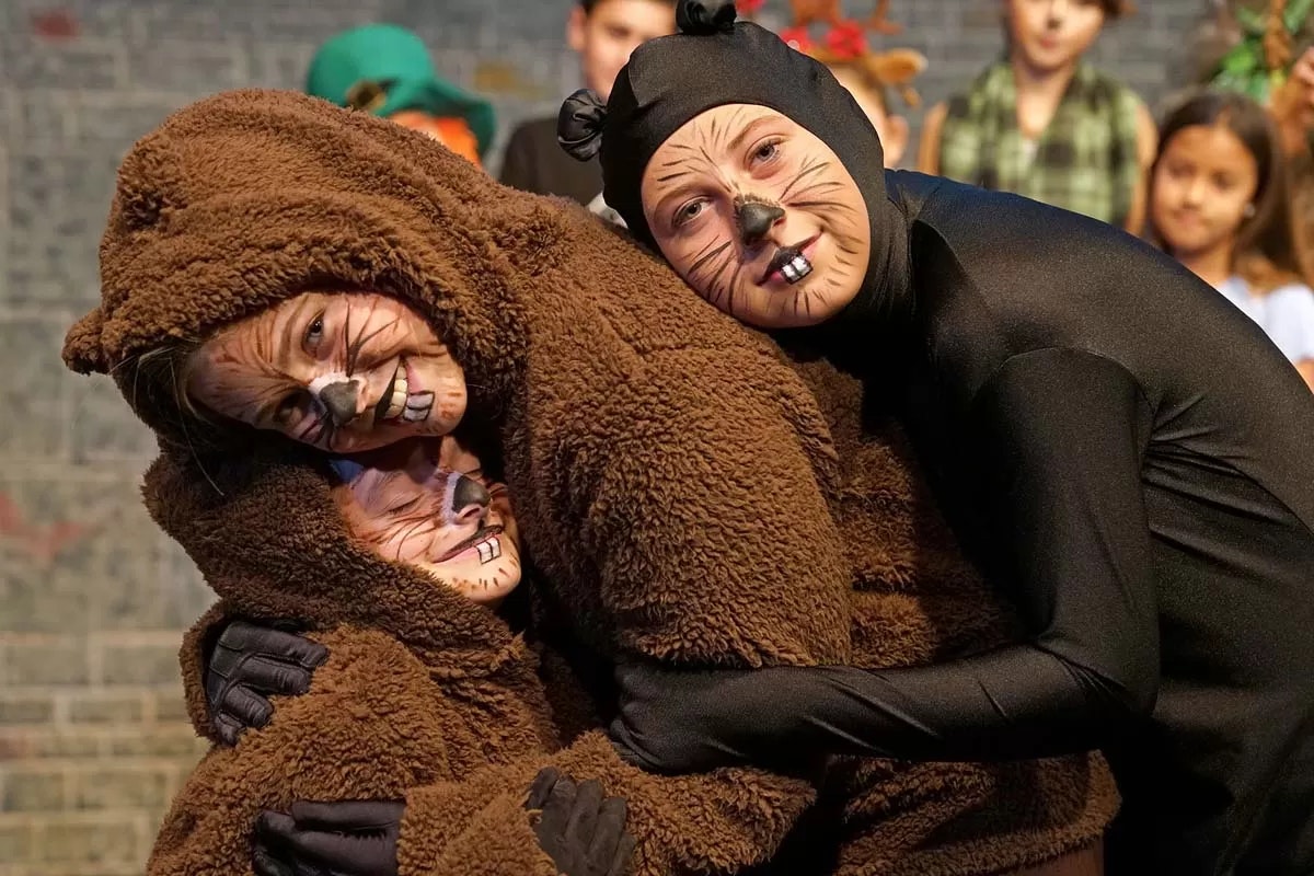 Three people dressed as animals, two in bear costumes and one in a black outfit, hugging and posing in front of an audience.