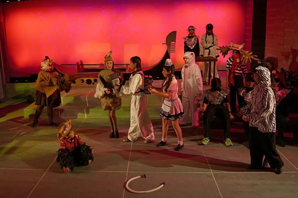 People in colorful costumes performing on stage with a vibrant red backdrop.