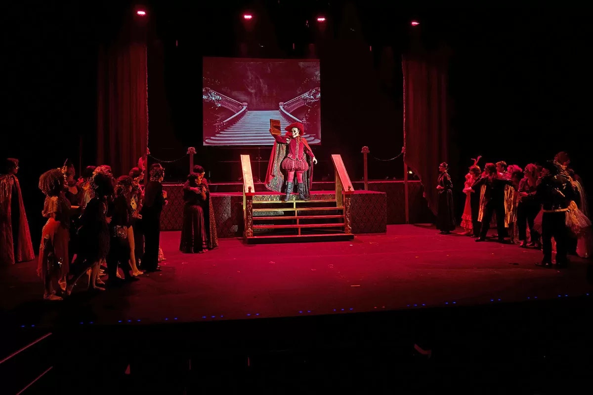 A theatrical performance with actors in costume on stage under red lighting.