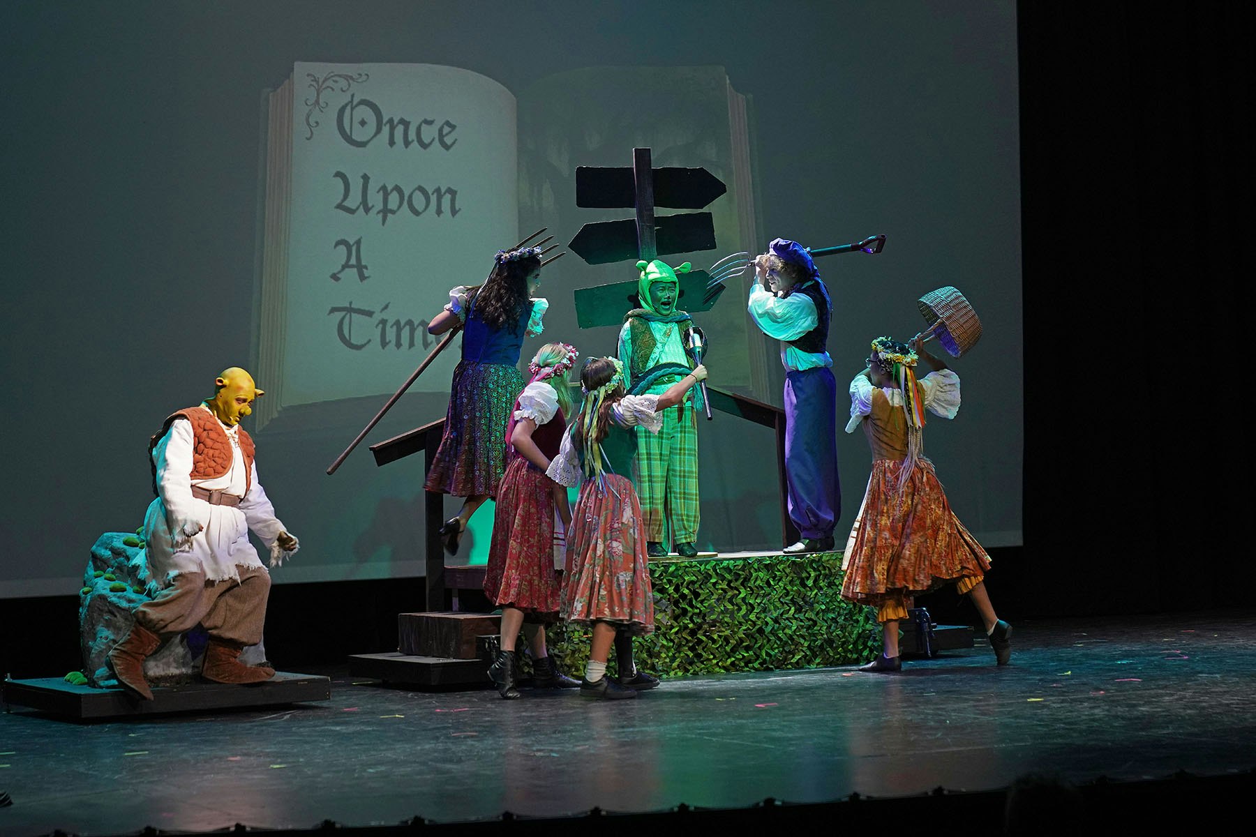 A stage play with characters in costume, featuring a fairytale theme and the phrase "Once Upon A Time" projected in the background.