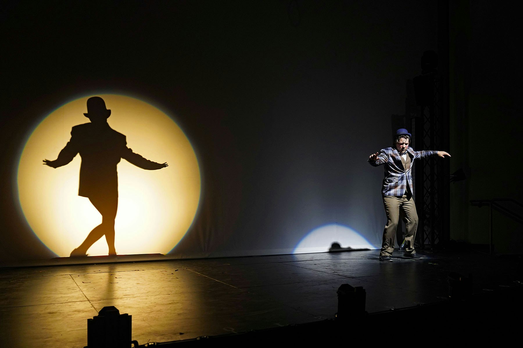 A performer on stage creates a striking shadow against a backdrop, showcasing a dynamic pose amidst dramatic lighting.
