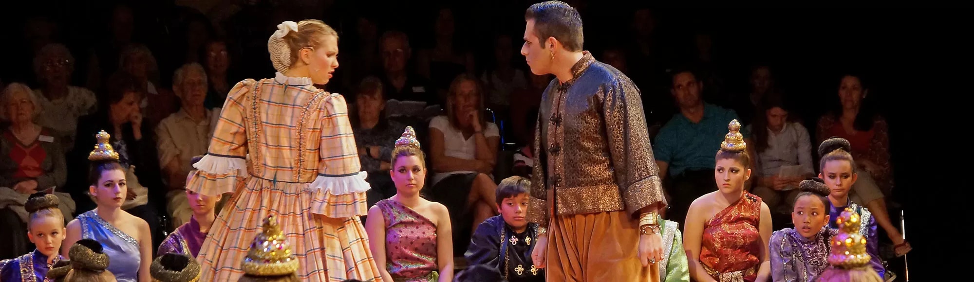 A theatrical performance with actors in historical costumes, children in ornate headpieces observe.