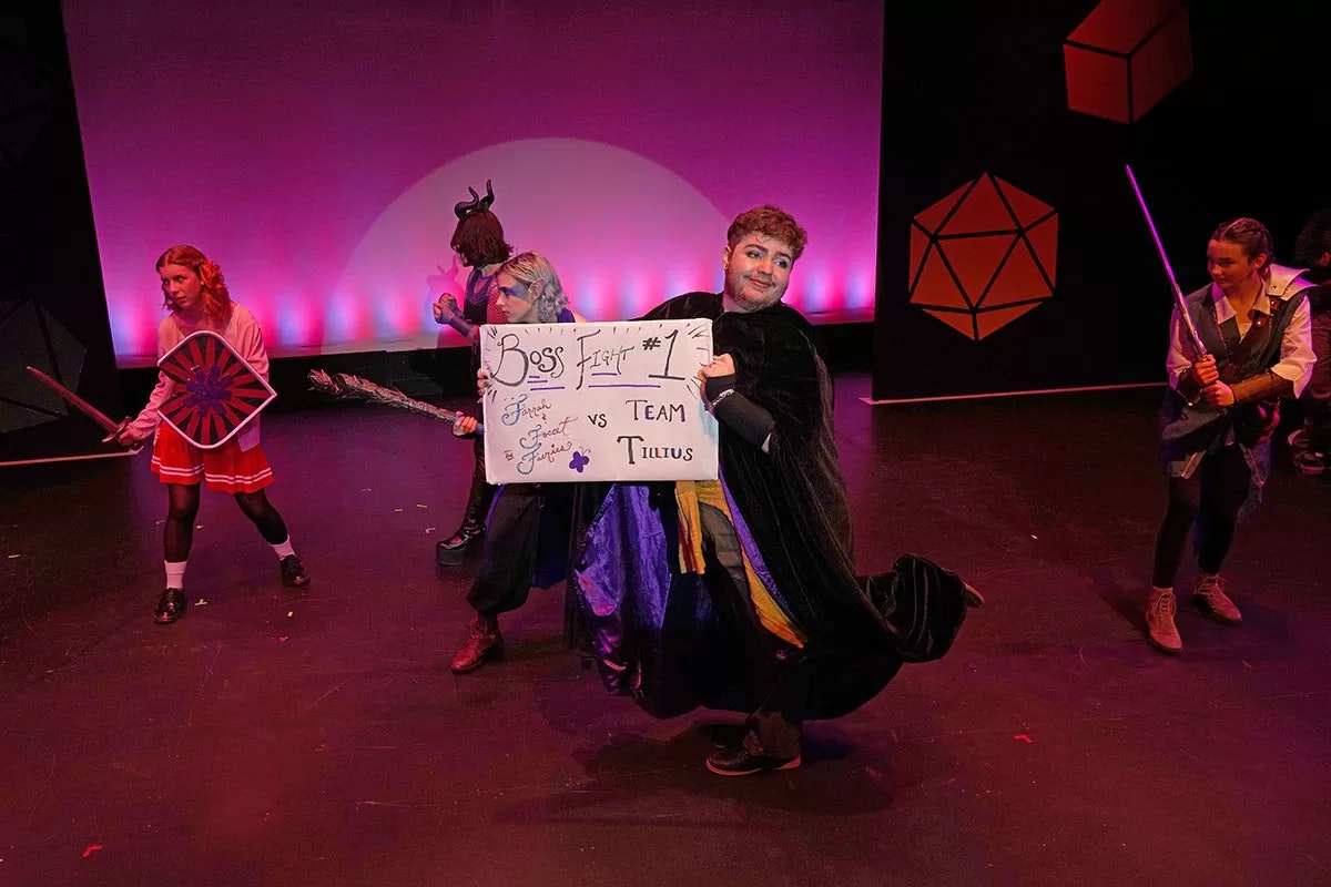 People in costumes on stage with swords and a sign reading "Boss Fight #1: Forest Forest Furries vs Team Tillius."