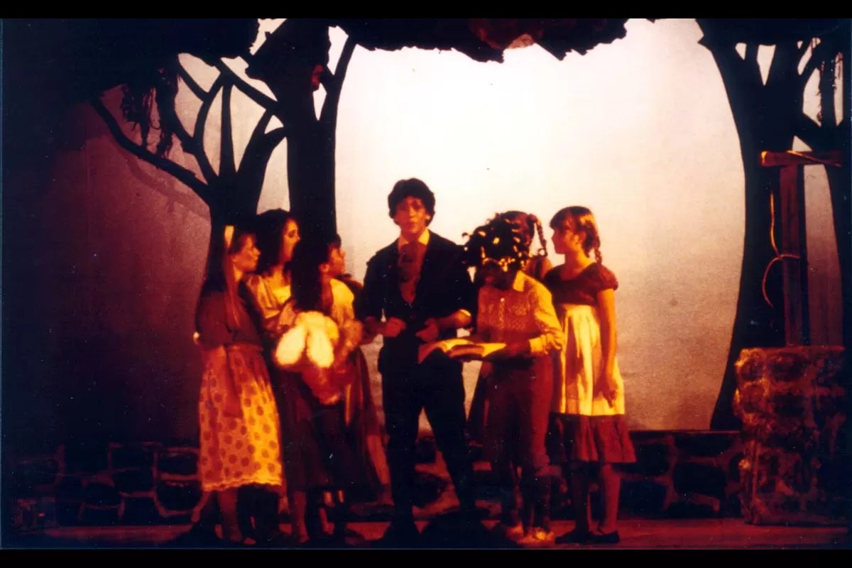 A group of people in costume are on a dimly lit stage set resembling a forest.