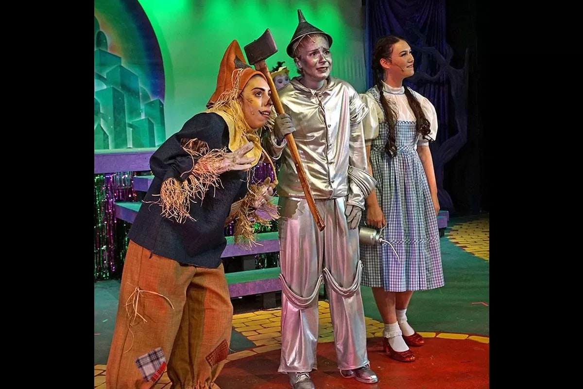Three people in costumes resembling characters from "The Wizard of Oz": Scarecrow, Tin Man, and Dorothy.