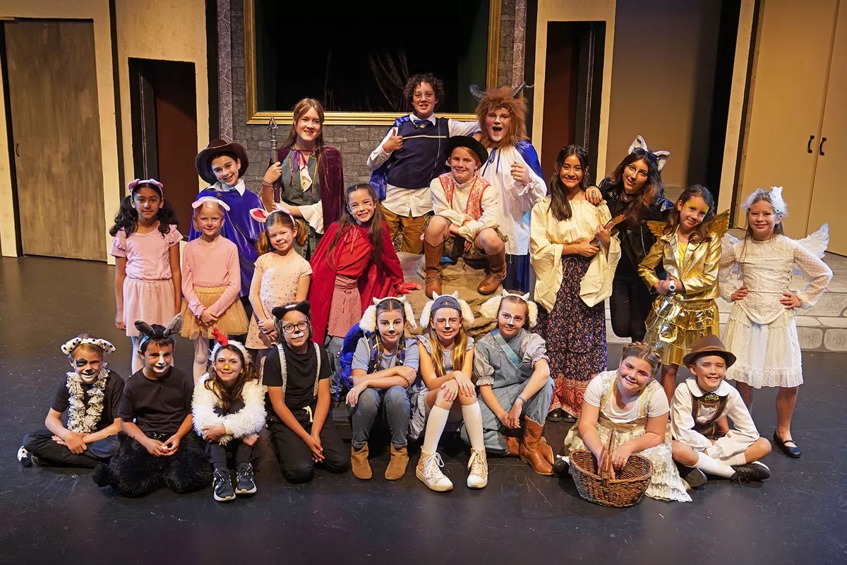 A group of children in colorful costumes posing on a stage for a theater production.