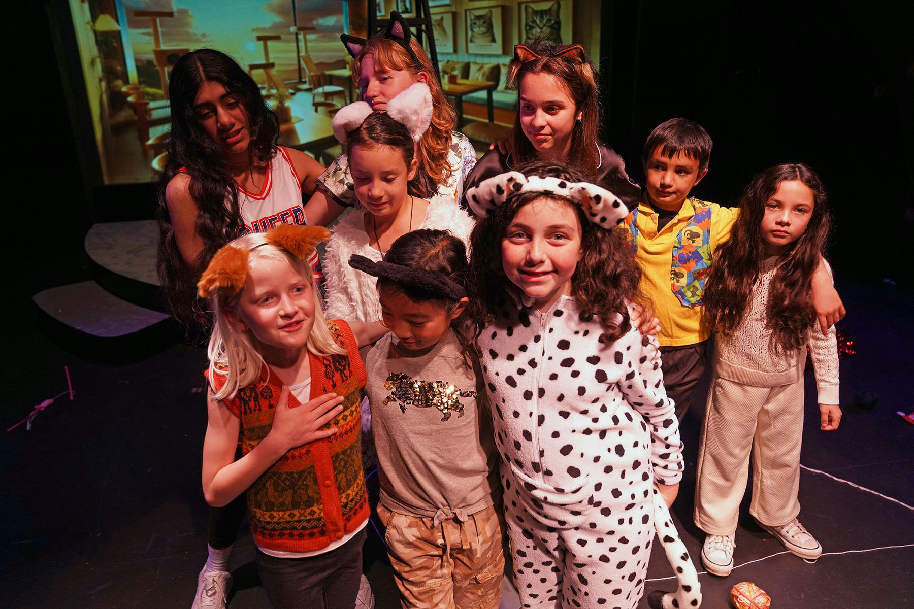 A group of kids in animal-themed costumes and accessories, smiling on stage.