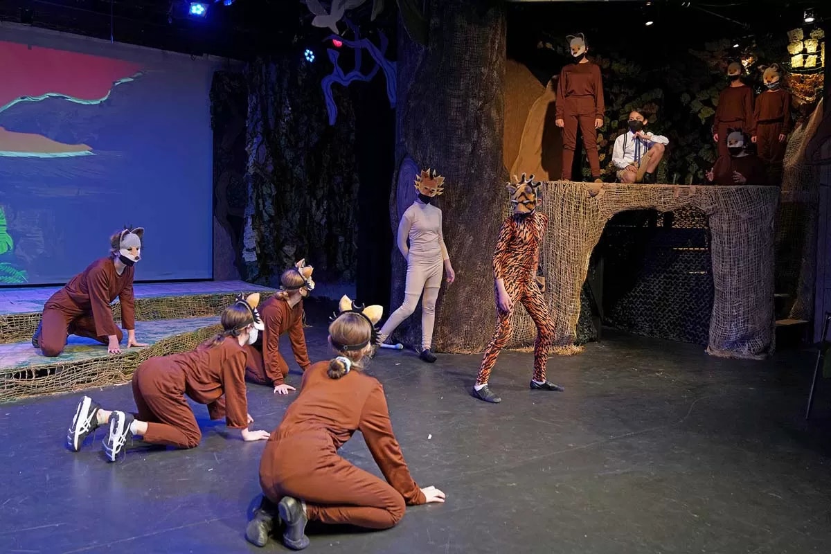 A stage performance with actors in animal costumes, including tigers and other creatures, engaging in a scene.