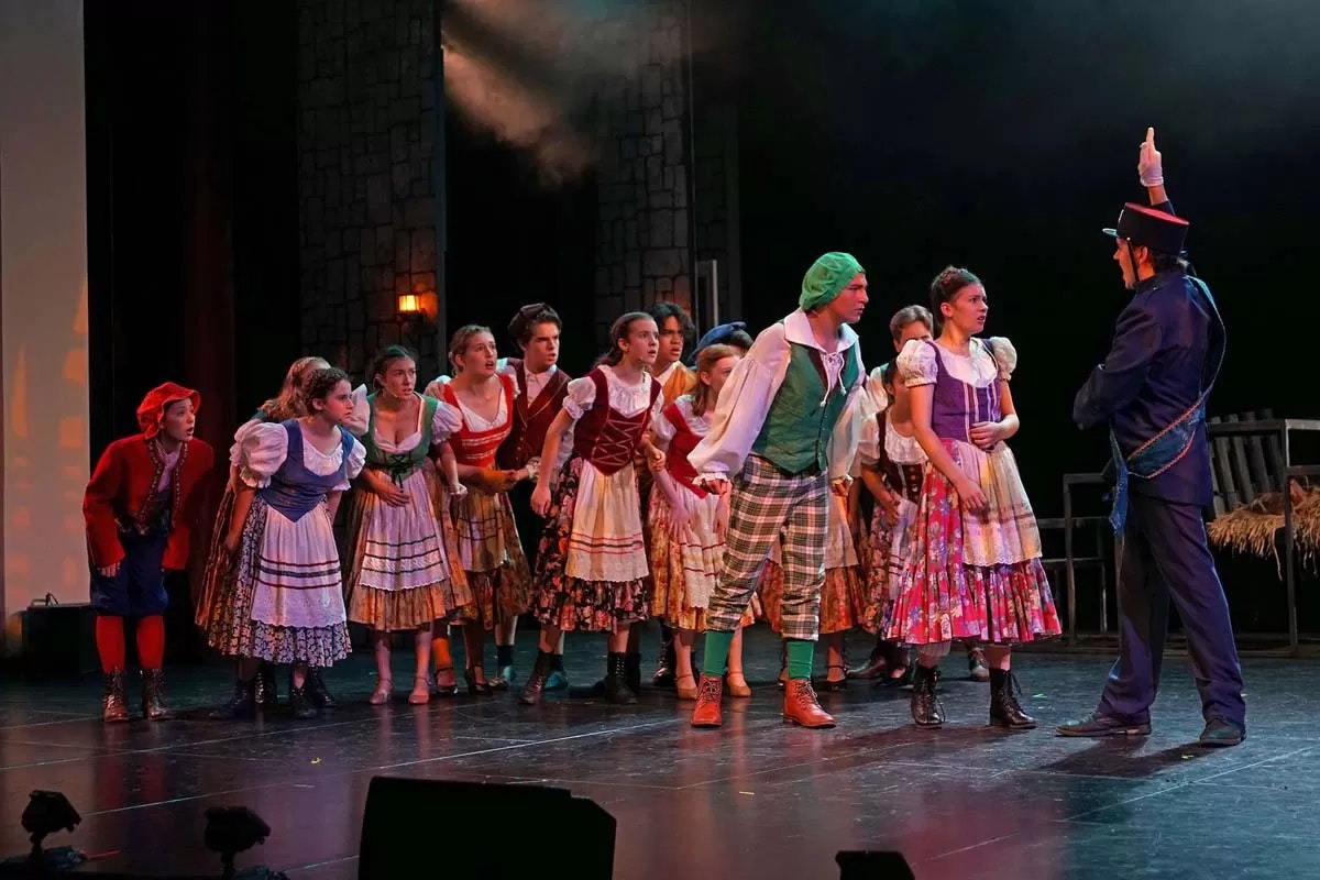 A theatrical performance with actors in colorful costumes, mid-scene interaction on stage.