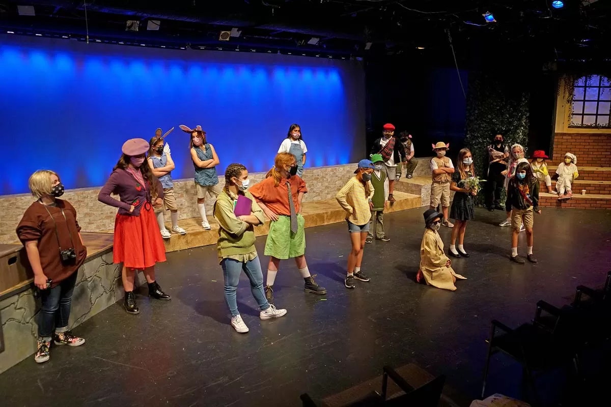 A group of people in costume and masks on a stage with a blue-lit background, arranged in various poses.