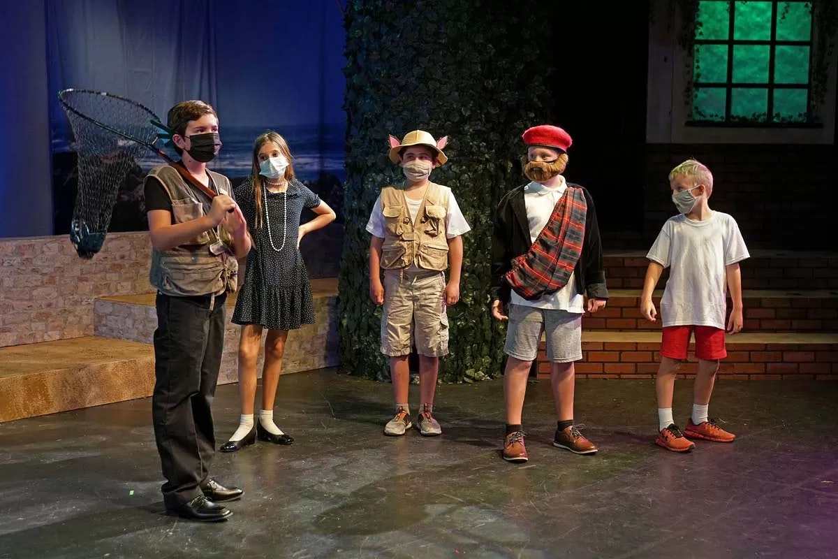 Children on stage wearing costumes and face masks, performing a play.