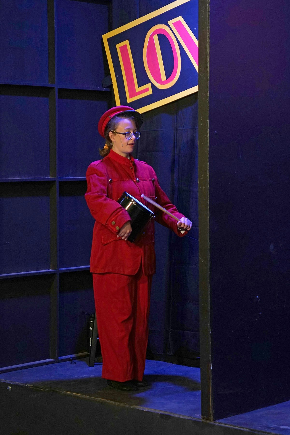 Person in a red uniform holding a drum, standing near a tilted "LOVE" sign.