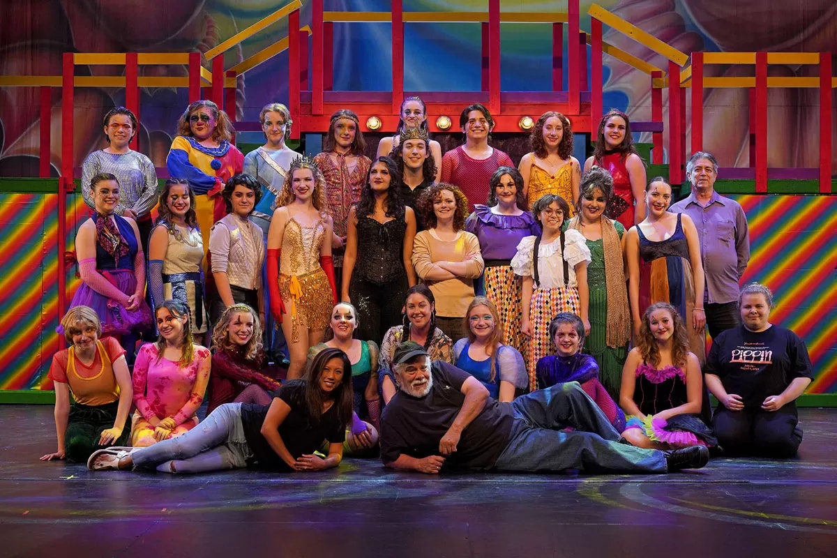 A group of people in colorful costumes posing on a stage with a vibrant set.