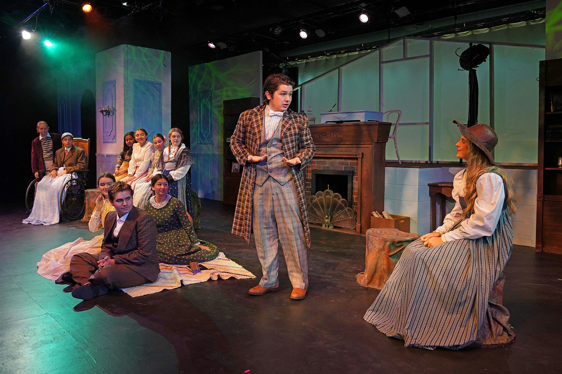 A stage scene with actors in historical costumes, performing a play. The setting includes furniture and a cozy atmosphere.