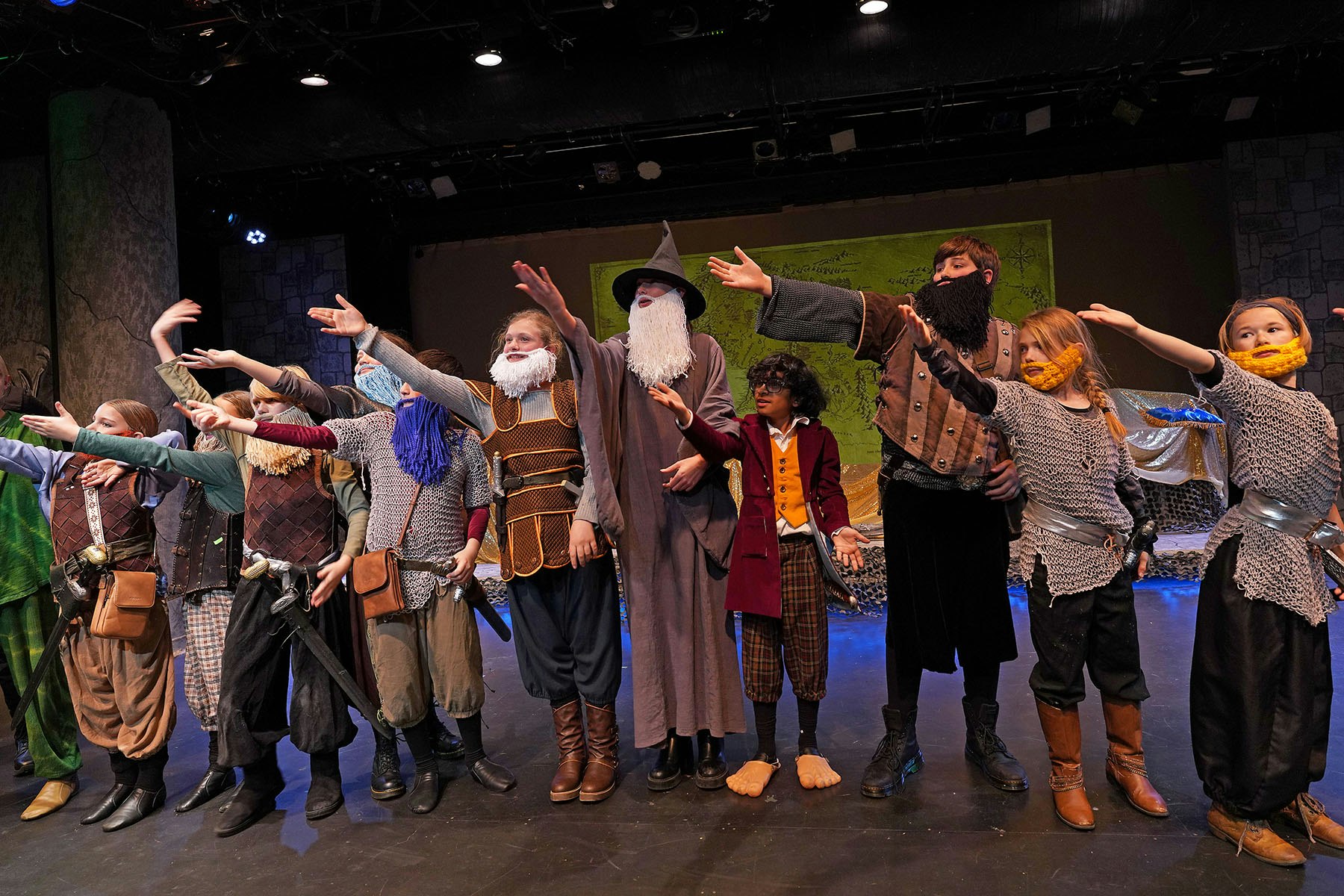 Children in fantasy costumes perform on stage, wearing fake beards and medieval attire.
