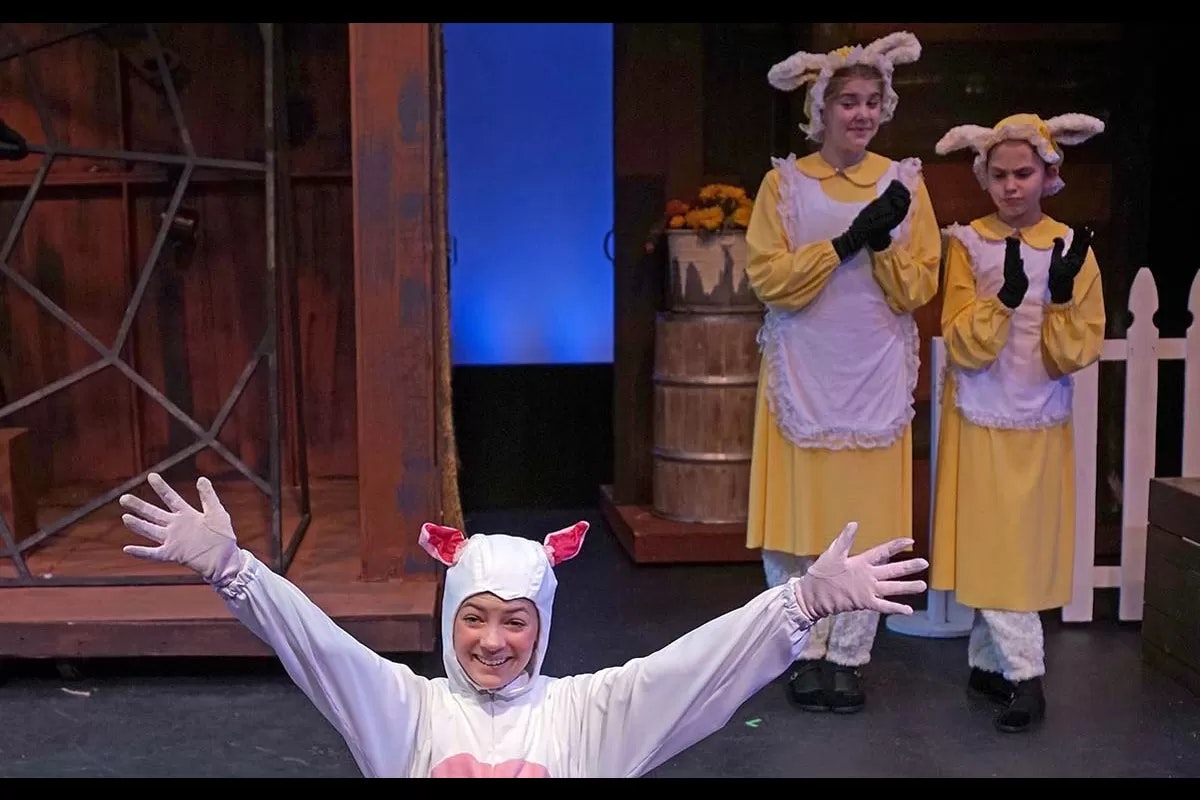 Three people in animal costumes, one in white with ears and two in yellow with fluffy ear headbands, on stage.