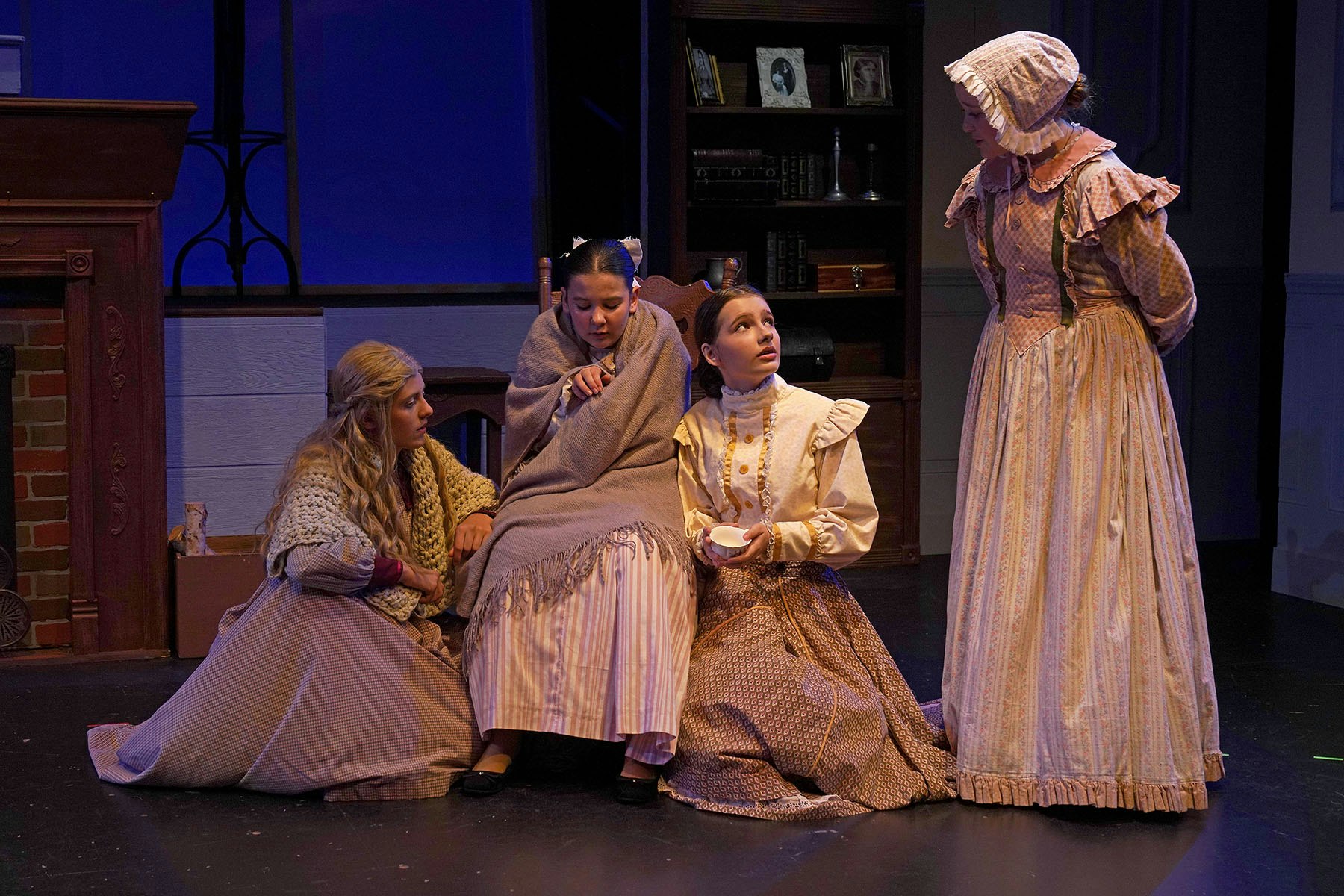 A scene from a play featuring four women in period costumes, with a warm, intimate setting and a focus on their interaction.
